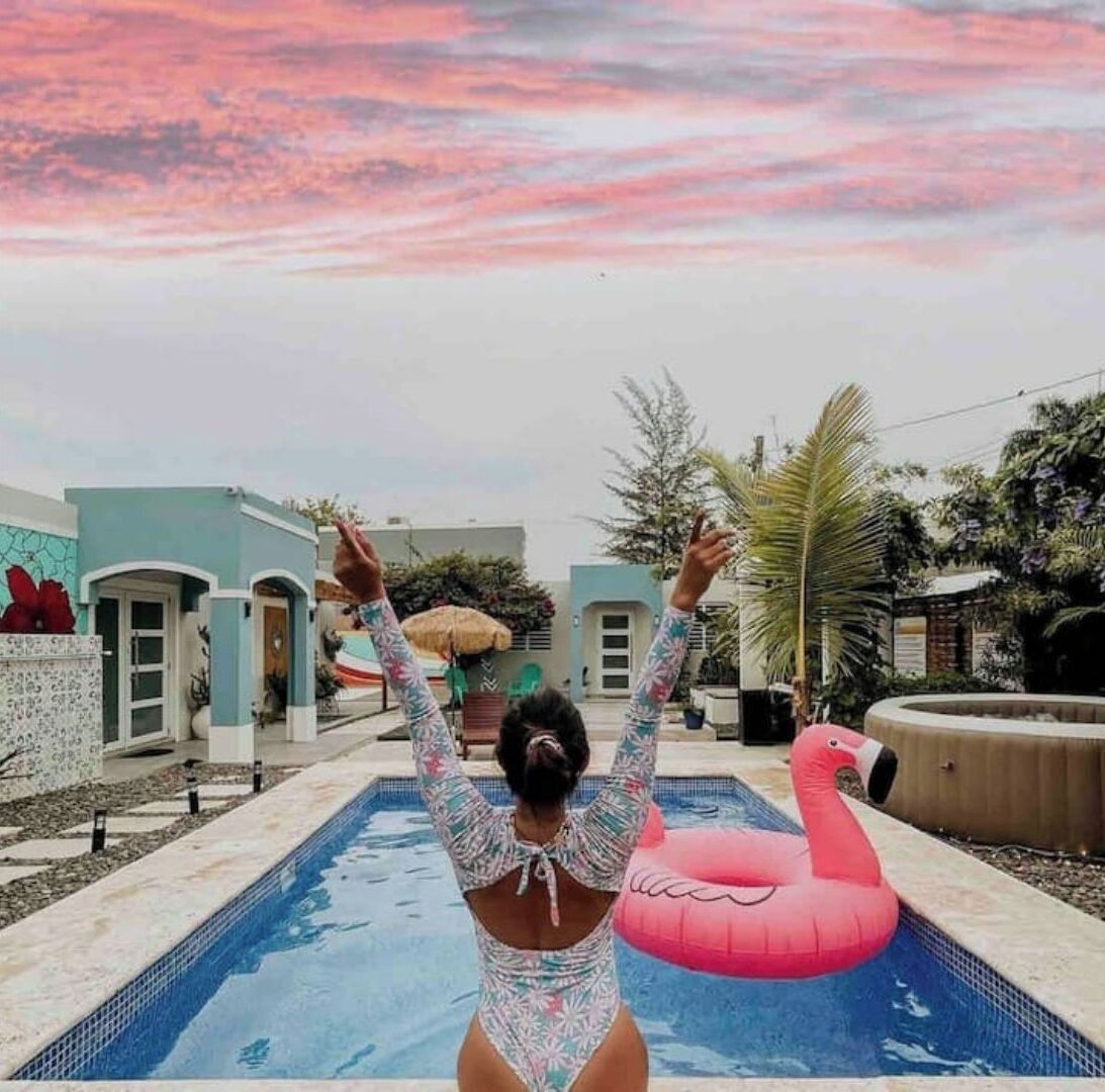 A swimming pool with a pink flamingo float, surrounded by a light blue building with a tiled exterior.