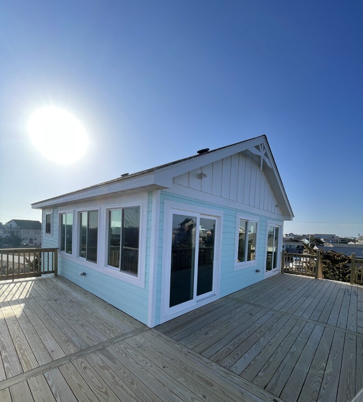 A small, single-story building with a light blue exterior and white trim, featuring large windows and a deck area.
