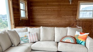 Ein gemütlicher Raum mit einem großen, beigefarbenen Ecksofa, einem Couchtisch aus Holz mit blau-weißem Meeresdesign und Holzwänden.