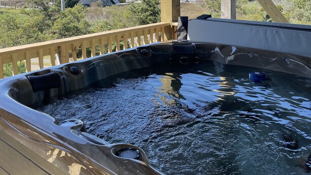 Ein Whirlpool unter einer Holzterrasse mit Blick auf Häuser und den Ozean.