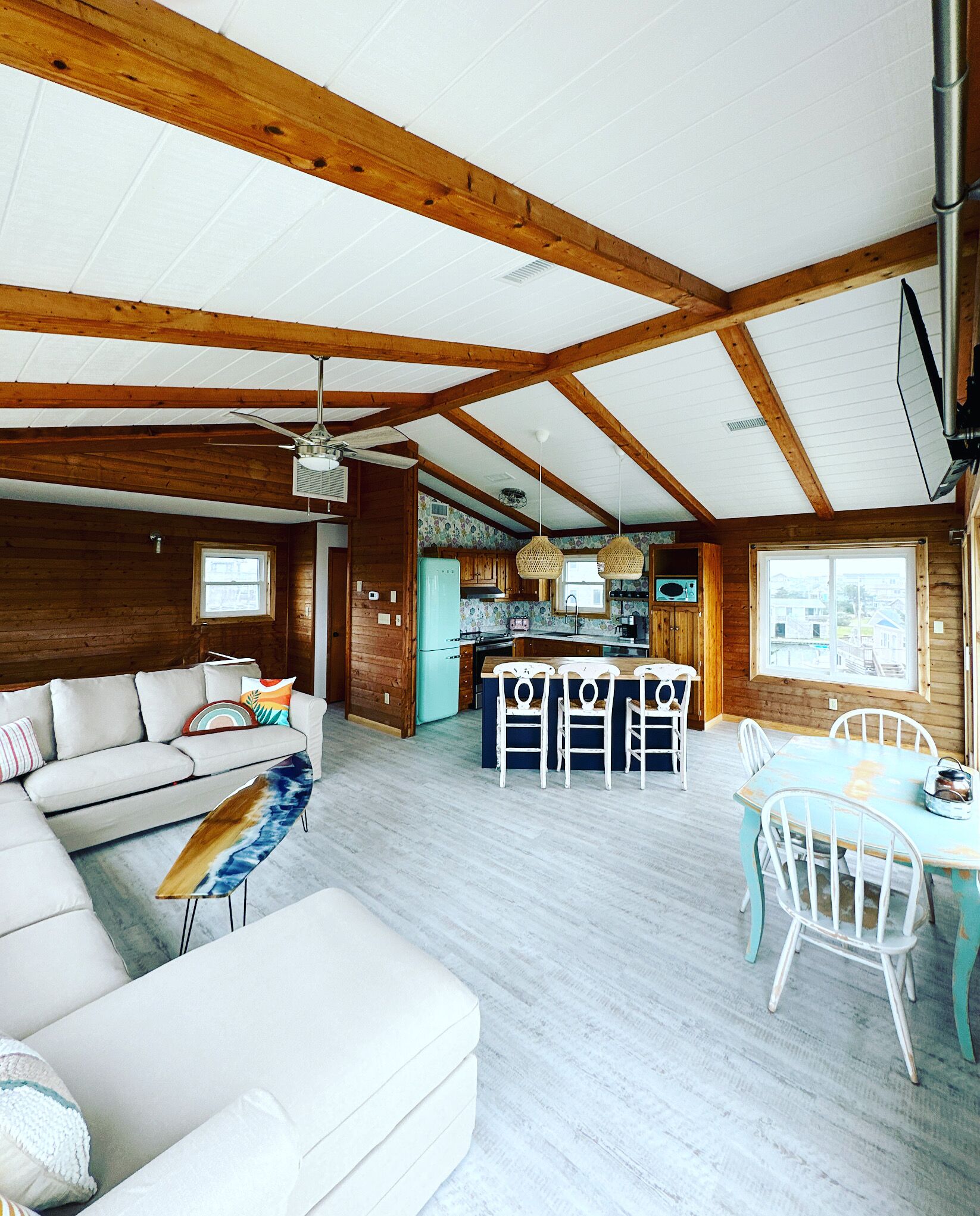 A spacious living area with a wooden ceiling, a kitchen with a refrigerator, and a dining area with chairs and a table.