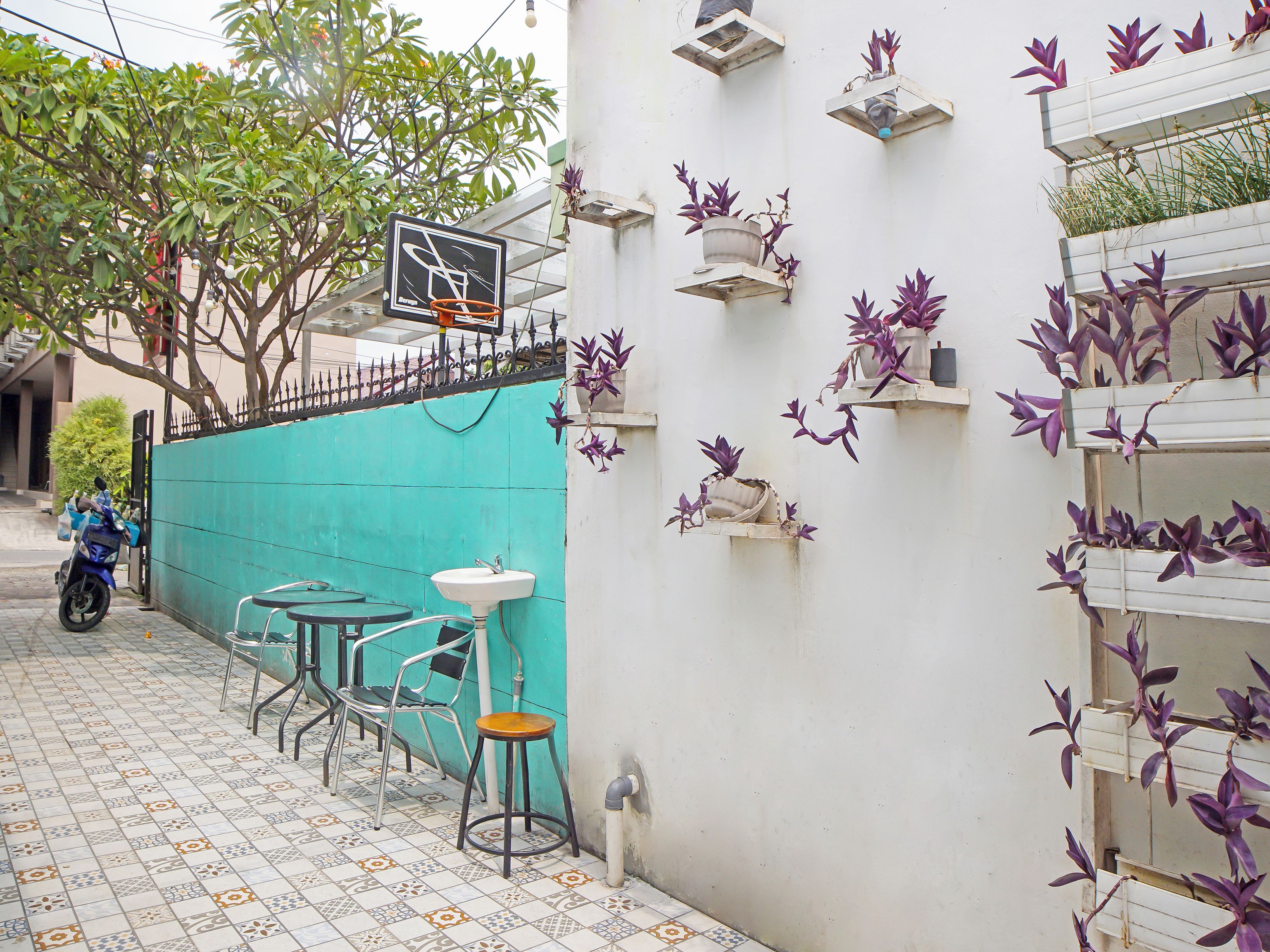 A narrow outdoor seating area with a tiled floor, metal chairs, a small table, and a wall-mounted sink.