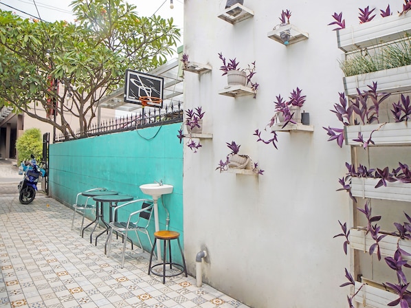 A narrow outdoor seating area with a tiled floor, metal chairs, a small table, and a wall-mounted sink. - OYO 91303 Puri Dennis (Medan)