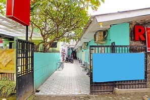 Un estrecho callejón con suelo de baldosas, un árbol que da sombra y un edificio con fachada verde y un letrero rojo.