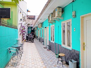 Un callejón estrecho con suelo de baldosas, una moto estacionada a la izquierda y una hilera de edificios con unidades de aire acondicionado y una puerta a la derecha.