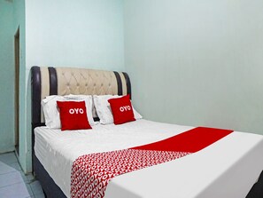 Een bed met een deken met een wit en rood patroon, twee rode kussens met de tekst 'OYO' erop, en een gestoffeerd hoofdbord.