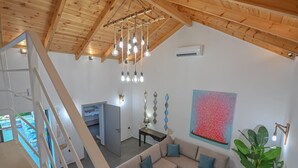 A modern interior with a wooden ceiling, a sofa with cushions, a dining table, a painting, and a staircase.
