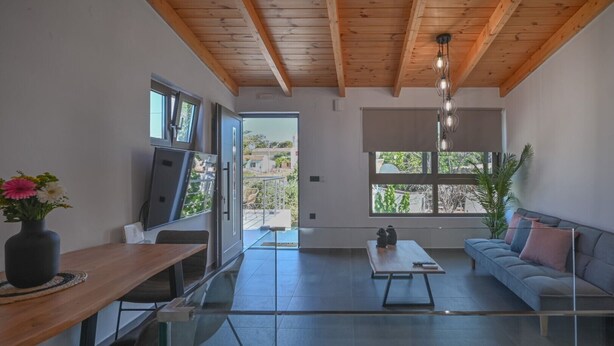 A modern living room with a wooden ceiling, a sofa, a coffee table, and a TV.