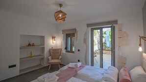 A bedroom with a bed, a chair, a shelf with toiletries, a window, and a door leading outside.