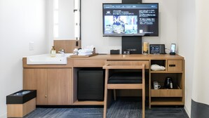 A modern hotel room with a wooden desk, a flat-screen TV, a sink, and a small trash bin.