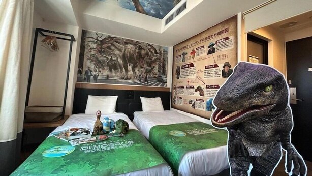 A hotel room with two beds, dinosaur-themed bedding, a mural, and a large dinosaur figure.
