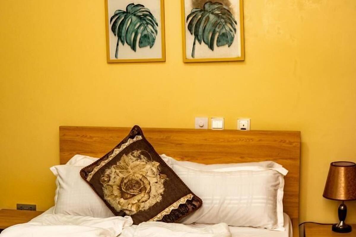 A hotel room with a bed, a nightstand, and two wall-mounted paintings of leaves.
