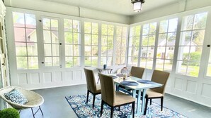 Une véranda avec une table à manger et des chaises, de grandes fenêtres et un tapis à motifs.