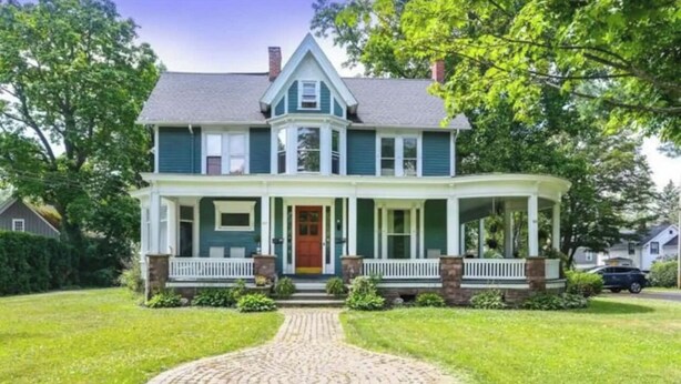 Une maison à deux étages avec un porche à l’avant, une entrée centrale et une allée menant à la porte d’entrée.