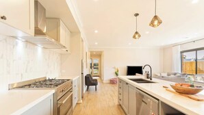 A modern kitchen with a stove, oven, and dishwasher, a large island with a sink, and pendant lighting. - Modern Beach House w/ BBQ & Family-Friendly Charm (Cowes)