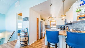 A modern kitchen with a wooden floor, blue bar stools, and a bar area. - La Carolina del Mar - KDH MP 5.5, 250 Yds to Beach, Ocean View, Hot Tub, Flex Stays (Kill Devil Hills)