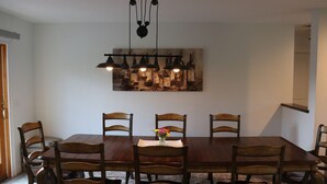 Un comedor con una gran mesa de madera, seis sillas, una lámpara colgante y una obra de arte en la pared.