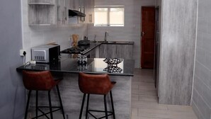 A modern kitchen with grey cabinets, a black countertop, and two bar stools. - Phakela Cottages (Jwaneng)