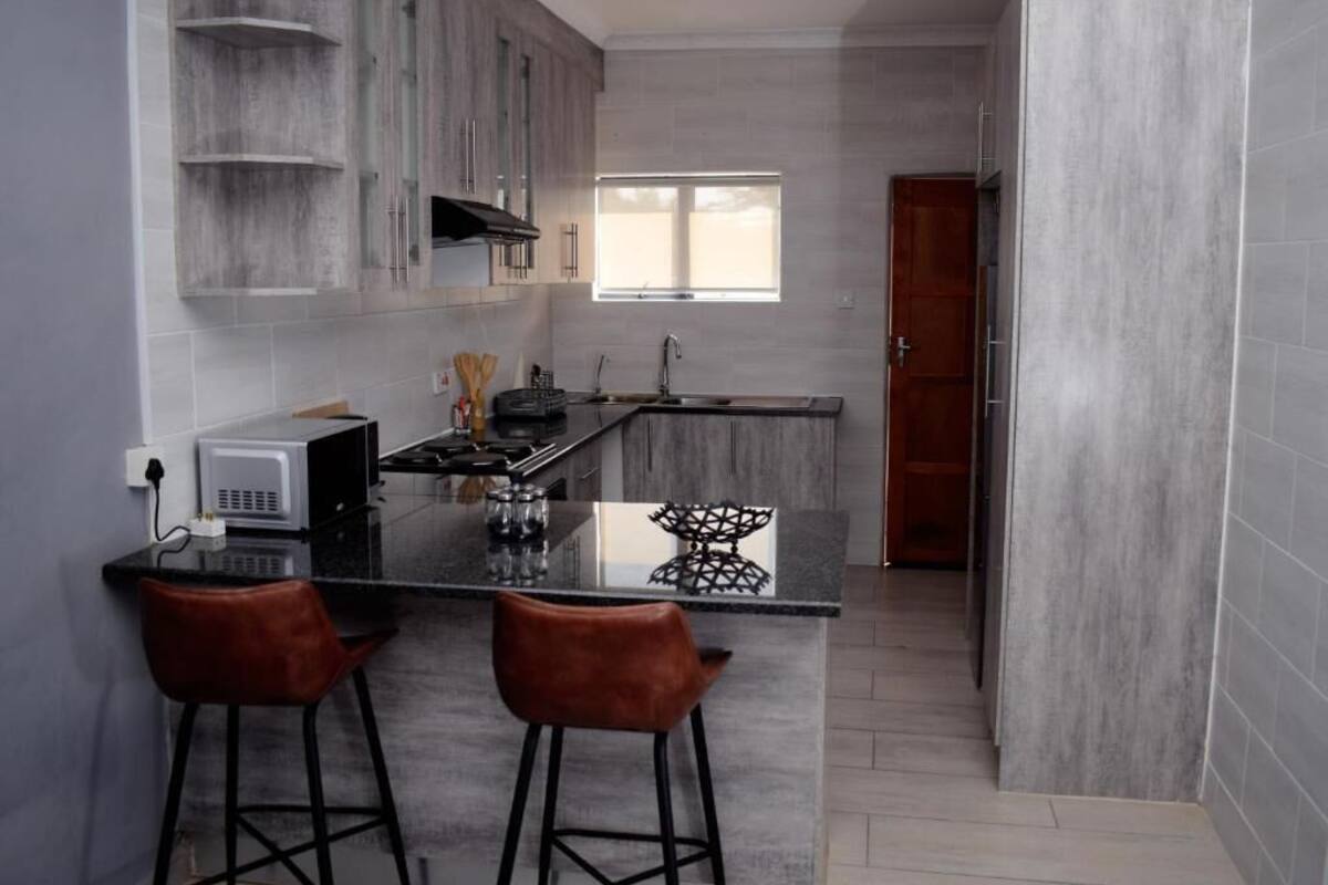 A modern kitchen with grey cabinets, a black countertop, and two bar stools.