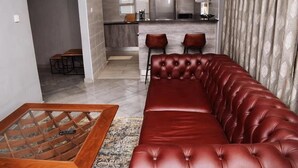 A modern living room with a red leather sofa, a wooden coffee table, and a kitchen in the background. - Phakela Cottages (Jwaneng)
