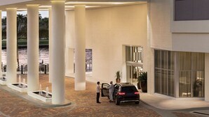 A modern hotel entrance with a covered outdoor area, columns, a car, and a body of water in the background. - Suite Ocean View w/JACUZZI, POOL, GYM and MORE (Hollywood)