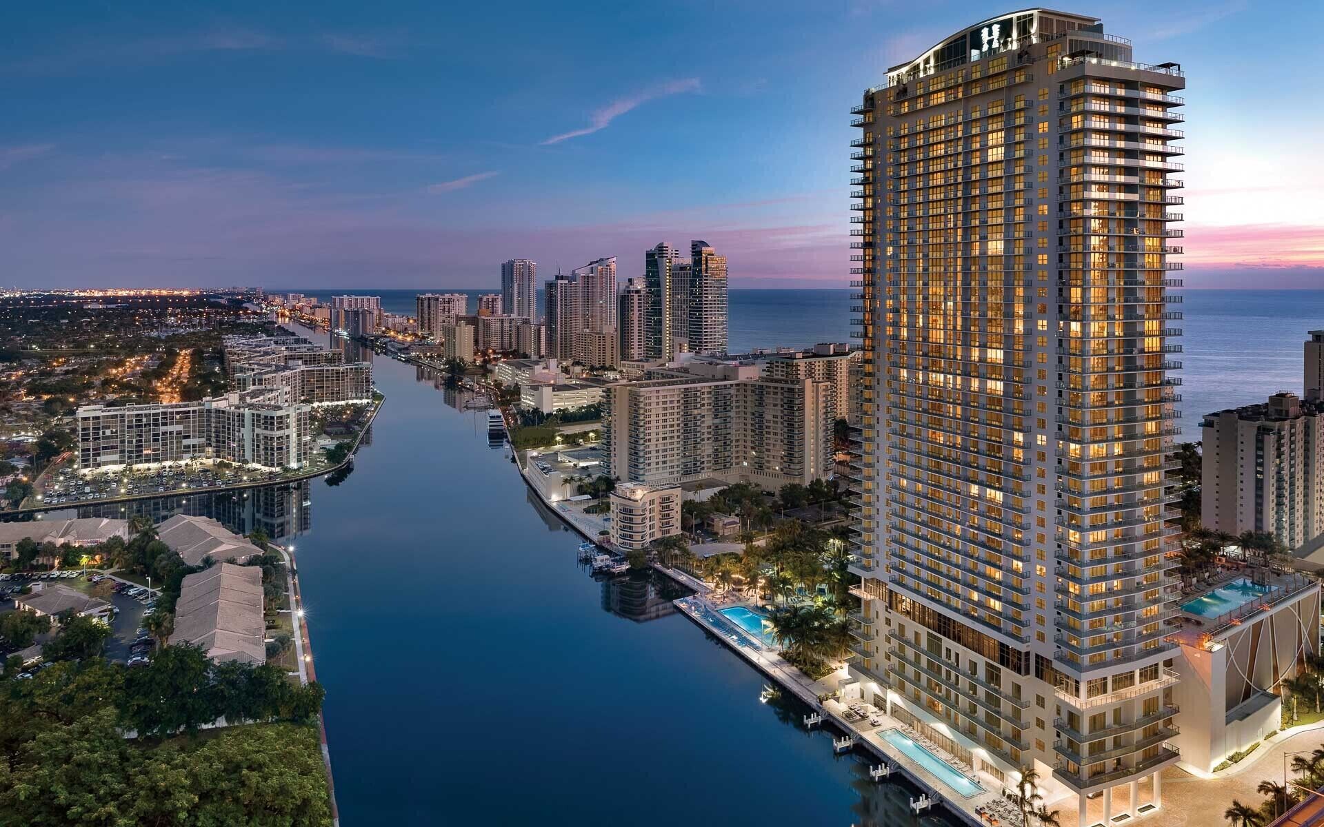 Een hoog hotel met meerdere verdiepingen, een zwembad en een jachthaven.