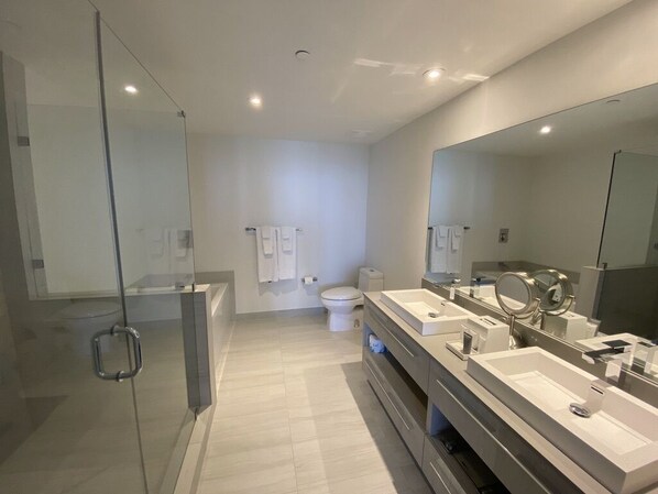 A modern bathroom with a glass shower enclosure, a large mirror, and a dual sink vanity. - Suite Ocean View w/JACUZZI, POOL, GYM and MORE (Hollywood)