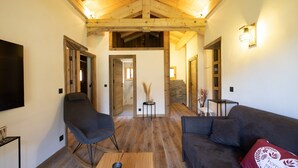 Ein modernes Wohnzimmer mit Holzboden, einem Flachbildfernseher, einer Couch, einem Schaukelstuhl und einem Couchtisch.