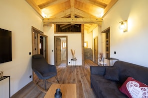 A modern living room with a wooden ceiling, a flat-screen TV, a sofa, a rocking chair, and a coffee table.