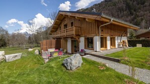 Ein zweigeschossiges Holzhaus mit Balkon, einer überdachten Sitzterrasse und Blick auf einen Berg.