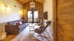 Ein gemütliches Wohnzimmer mit Holzboden, einem Sofa, einem Schaukelstuhl, einem Fernseher und einer großen Holztür.