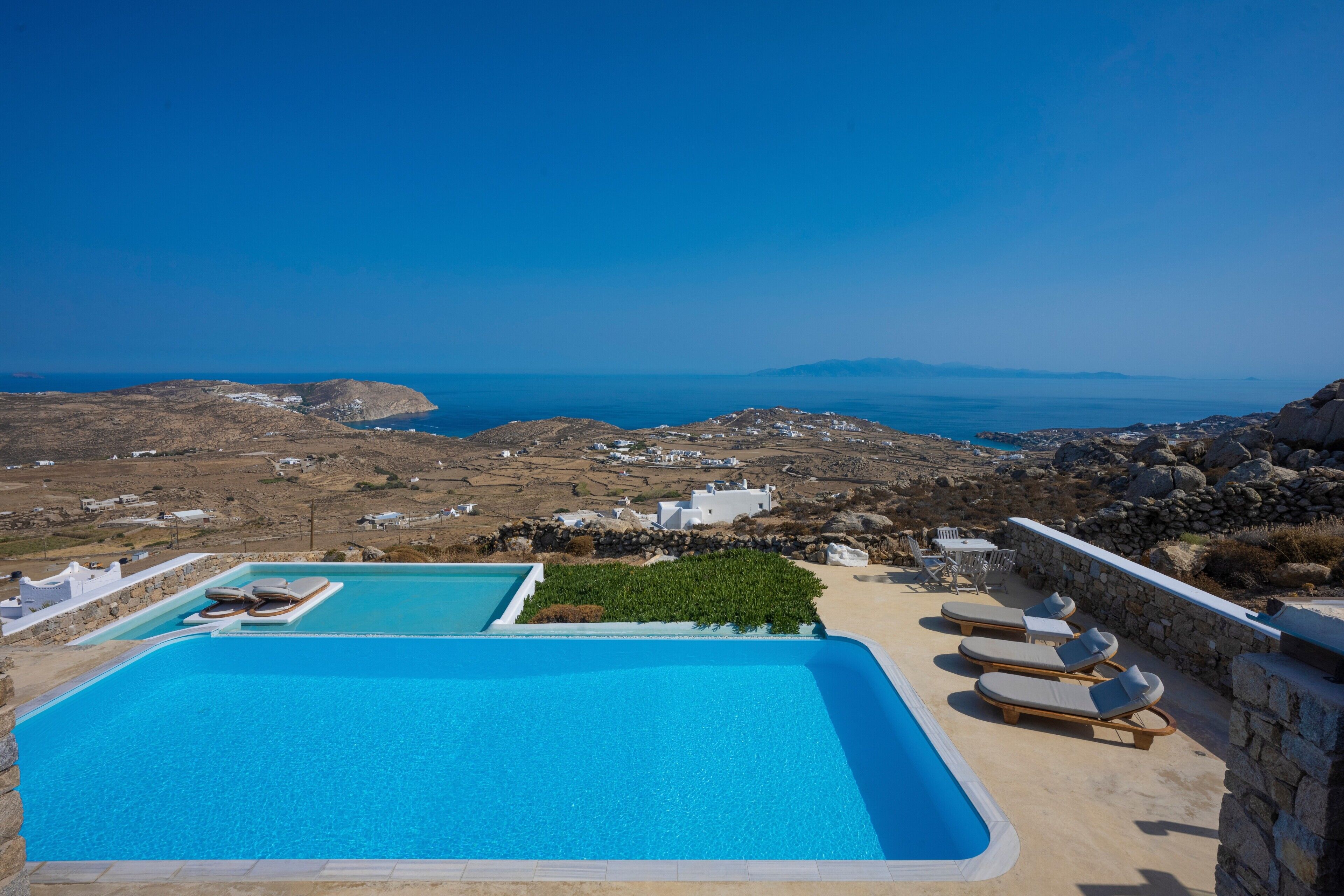 A pool area with lounge chairs and a view of the sea and landscape.