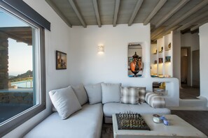 Una sala de estar moderna con un ventanal grande, un sofá modular, un tablero de ajedrez y una estantería.