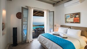 Um quarto com cama, vista para o mar, área de refeições e uma pintura grande na parede.