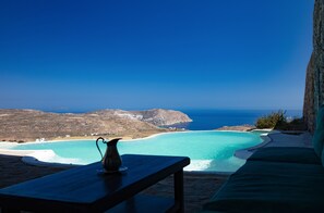 Une vue sur la mer, avec une table et une chaise, un ciel bleu dégagé et une côte lointaine.