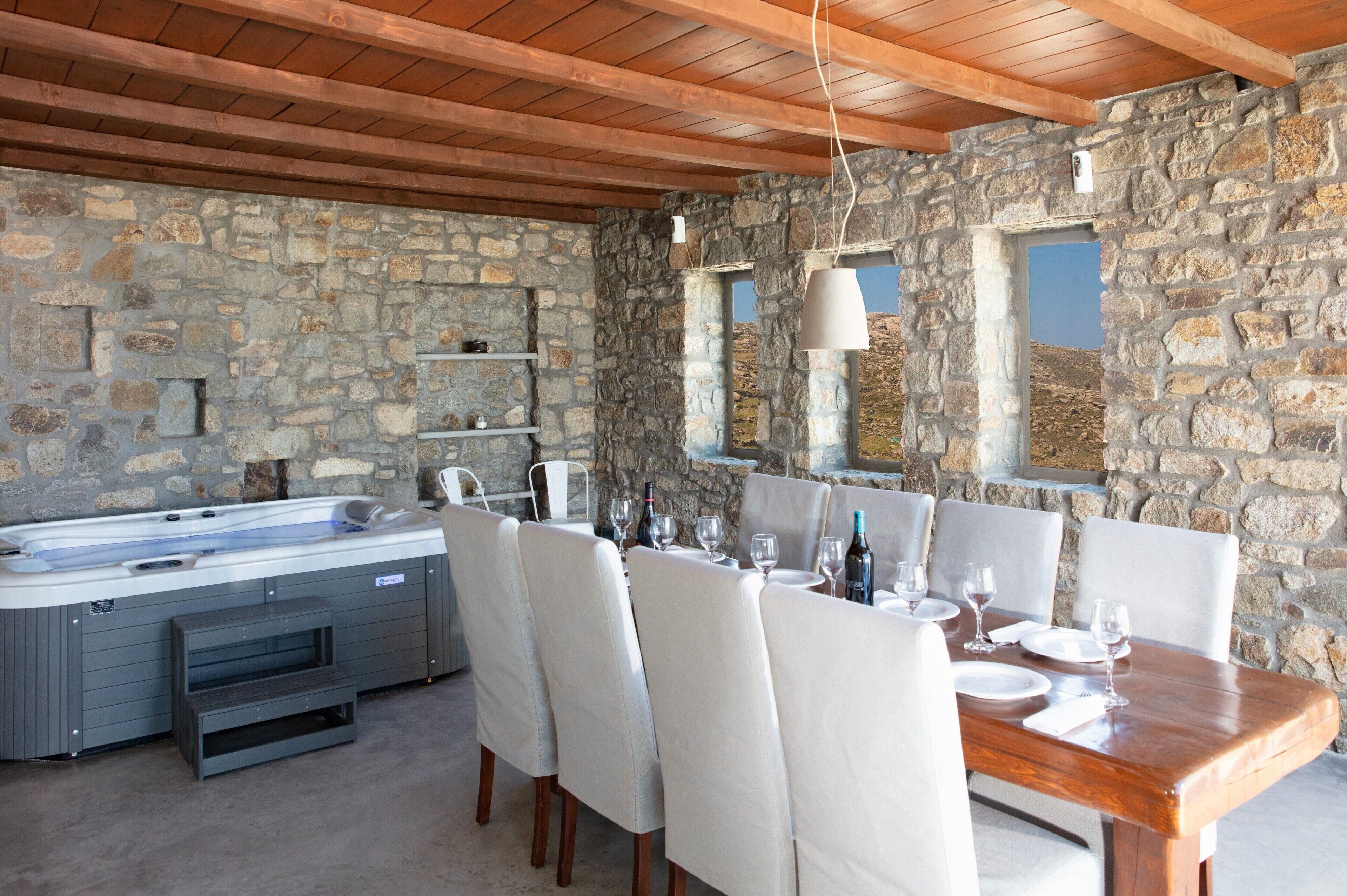 Habitación con paredes de piedra, bañera de hidromasaje, mesa de comedor y sillas.