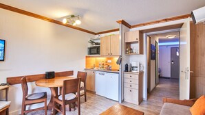 Une cuisine compacte équipée d’un four à micro-ondes, d’un évier et de placards en bois. On y trouve également un coin repas avec une table et des chaises, ainsi qu’un canapé agrémenté d’un coussin orange.