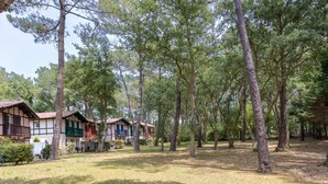 A row of traditional wooden cabins with sloped roofs, surrounded by a forested area. - Villa 'Christine' with Shared Pool, Shared Garden, and Balcony (Moliets-et-Maa)