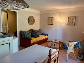 A cozy room with a bed, a dining table, a small round table, a wicker chair, a clock, and framed pictures on the wall. - Villa 'Christine' with Shared Pool, Shared Garden, and Balcony (Moliets-et-Maa)