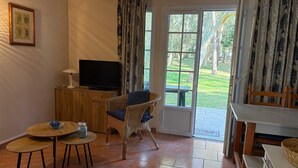 A room with a television, wicker chairs, a small table, a door leading outside, and a framed picture on the wall. - Villa 'Christine' with Shared Pool, Shared Garden, and Balcony (Moliets-et-Maa)
