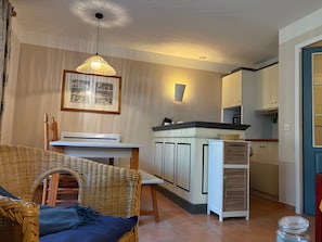 A compact kitchen with a dining area, a wicker chair, a pendant light, and a framed picture on the wall. - Villa 'Christine' with Shared Pool, Shared Garden, and Balcony (Moliets-et-Maa)