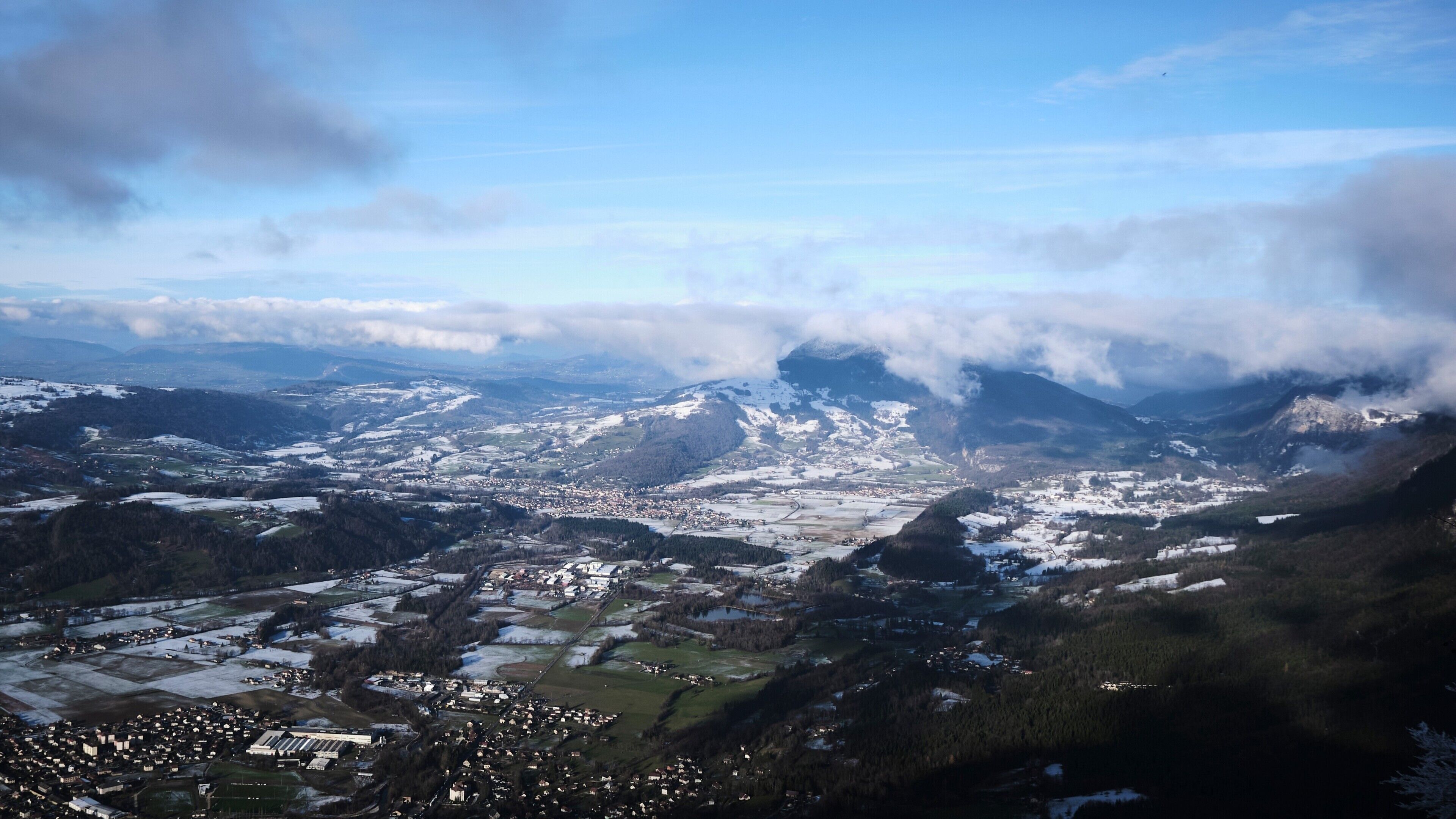 Un paysage montagneux avec une ville nichée dans une vallée, entourée de collines et de forêts couvertes de neige.