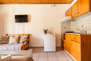 A compact room with a bed, a small refrigerator, wooden cabinets, a tiled backsplash, and a mounted television. - Apartment 'Marketos  Maisonette  4pax' with Mountain View, Wi-Fi and Air Conditioning (Kefalonia)