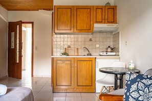 Een kleine keuken met houten kastjes, een wit aanrecht en een eethoekje met een tafel en stoelen.