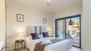 Habitación de hotel con cama, dos mesitas de noche con lámparas, una silla y vistas a un área exterior.
