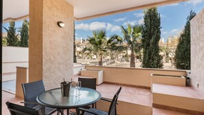 Un balcón con una mesa y sillas de vidrio, una botella de champán y vistas a palmeras y edificios.