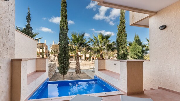 Un área de piscina con dos sillas de descanso, una piscina azul cristalina y palmeras que la rodean.