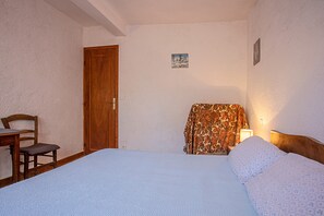 Una camera da letto con un letto, una sedia, una porta in legno e un piccolo quadro appeso al muro.