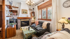 A cozy living room with a fireplace, a sofa, a table with a checkered tablecloth, and a bookshelf.