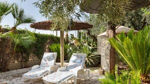 A patio with two sun loungers, a stone floor, and a variety of plants.